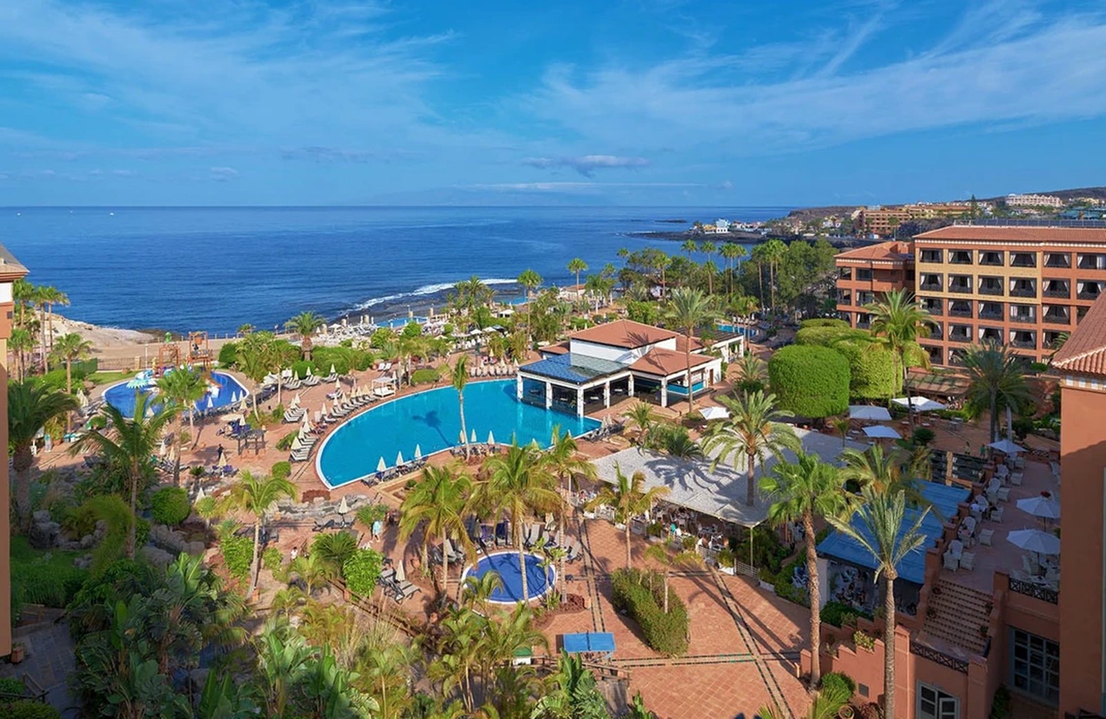 H10 Costa Adeje Palace seen from above: terracotta blocks and pool terraces set between palm gardens and the Atlantic at Playa La Enramada in La Caleta.