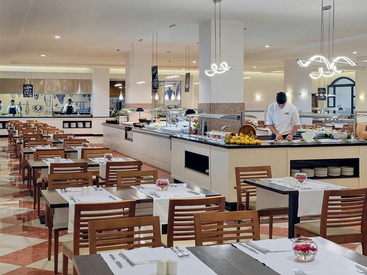 Buffet restaurant with a show-cooking counter, a chef at work and wooden dining tables set out under pendant lights.