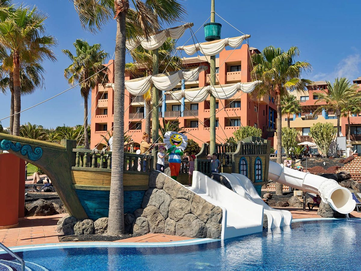 The children's pool built around a wooden pirate ship with white water slides, palms and resort buildings behind.