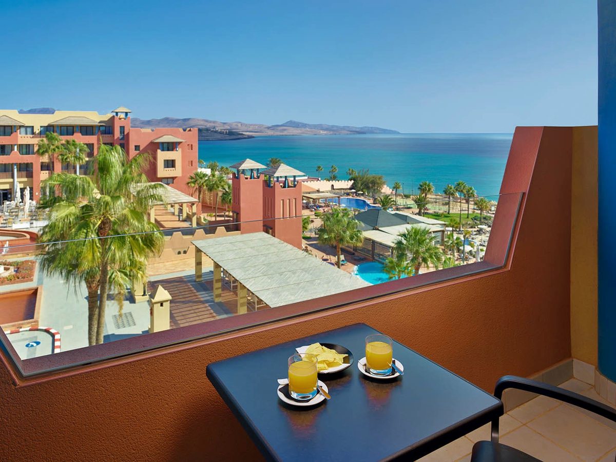 A private balcony with a small table, looking out over palms and the resort to the Atlantic.