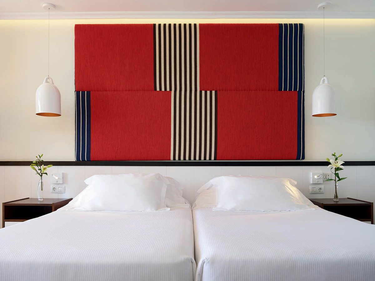A room with two single beds pushed together under a red striped headboard, with bedside pendant lamps.
