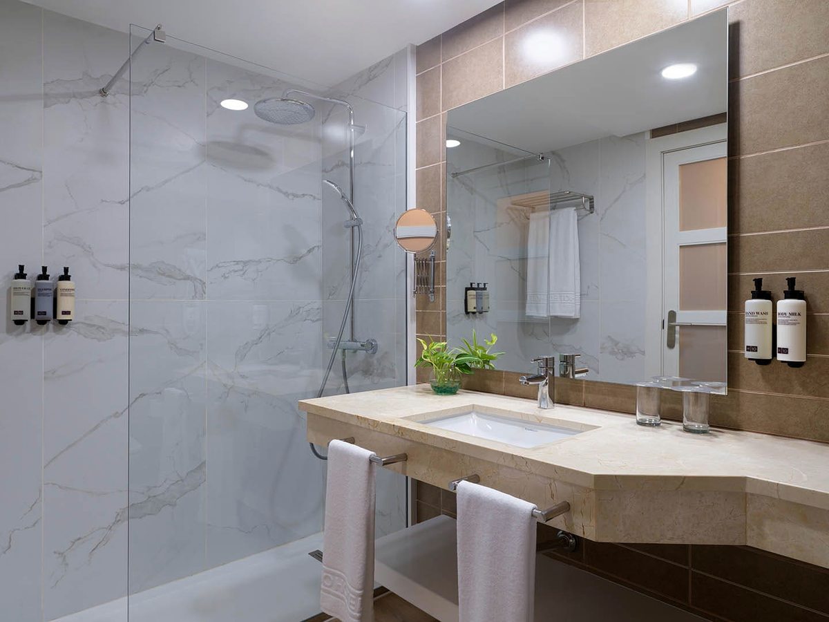 A room bathroom with a walk-in glass shower, a rain head and a stone vanity with a large mirror.