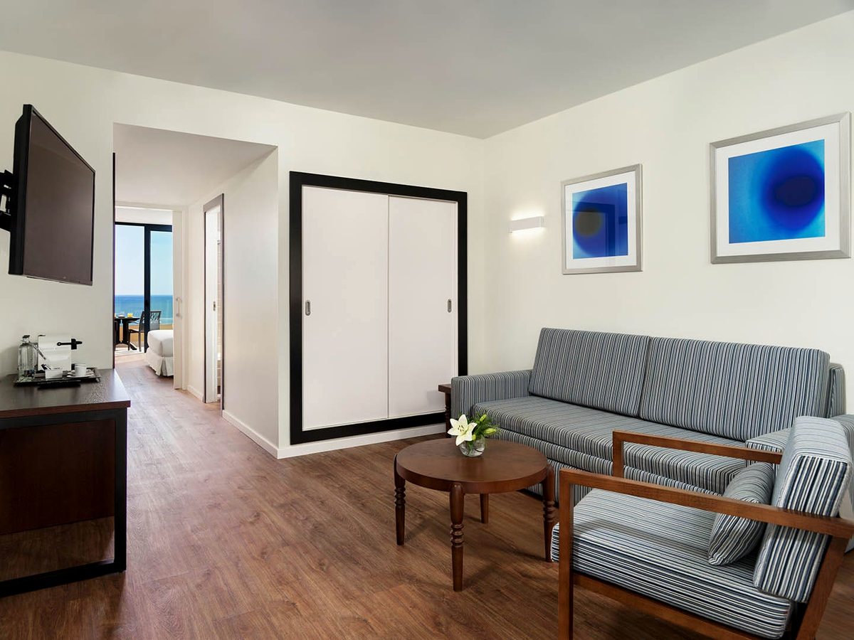 A suite living room with a striped sofa bed, armchair and television, the separate bedroom visible beyond.
