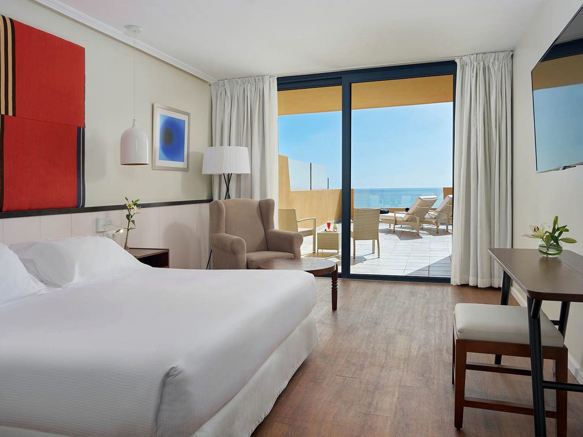 A sea-view room with a double bed and armchair, sliding doors open to a private terrace with sun loungers.