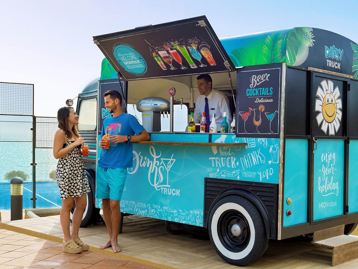 A turquoise vintage-style drinks truck on the pool deck, with two guests ordering at the hatch.