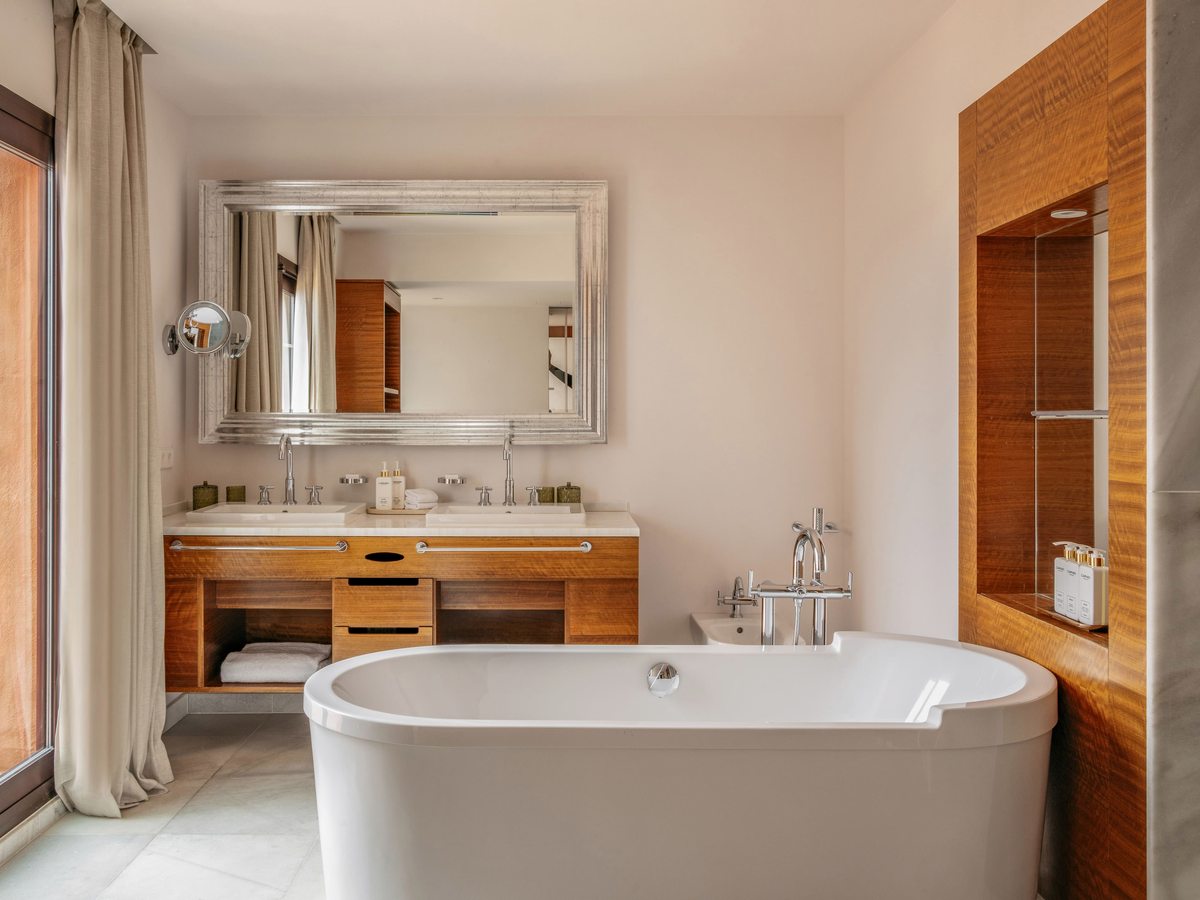 A bathroom with a freestanding oval bath, a wooden double vanity and a large mirror.