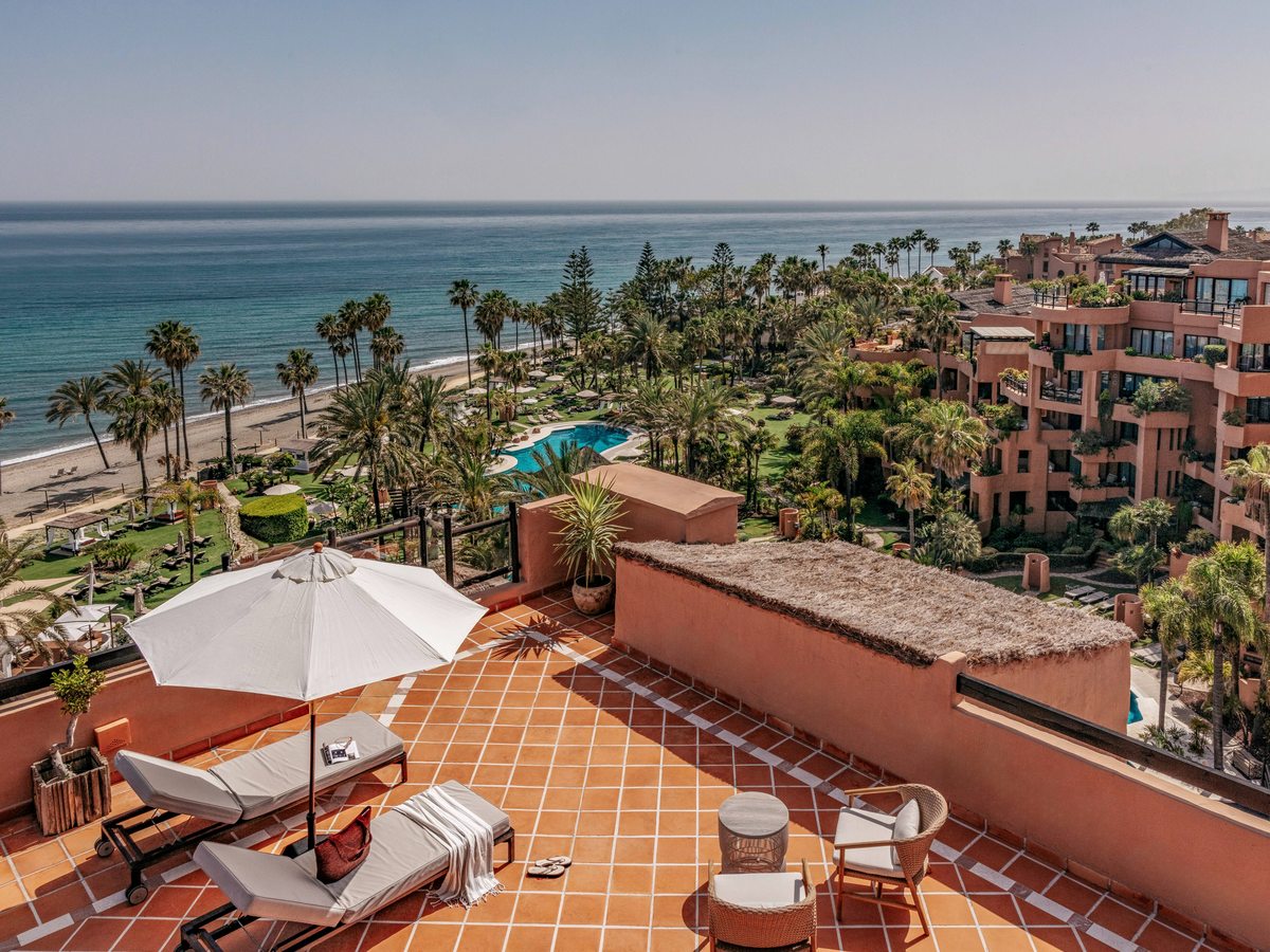 An elevated view over the resort's palm gardens and a free-form pool down to the beach and the sea.