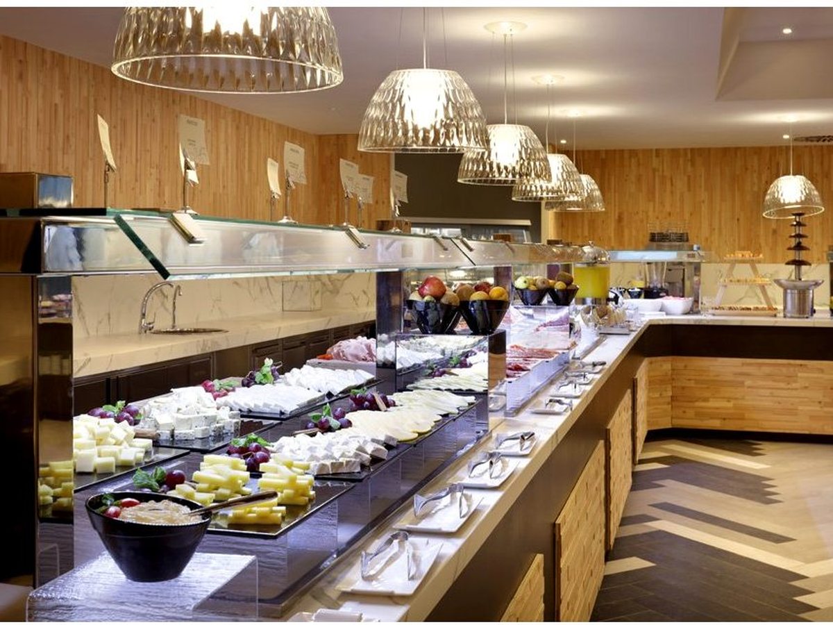 Buffet counter at Sessions with plated desserts and fresh fruit behind glass guards, under wooden pendant lights.