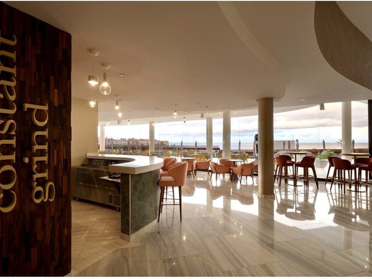 The Constant Grind coffee shop and bar with a counter, bar stools and orange chairs beside floor-to-ceiling windows onto the terrace.
