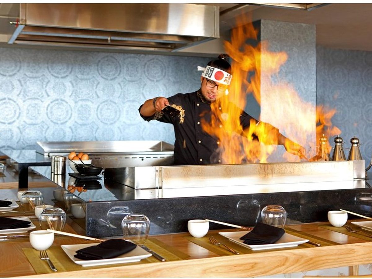A chef cooking over a flaming teppanyaki hotplate at a laid dining counter in the Asian restaurant.