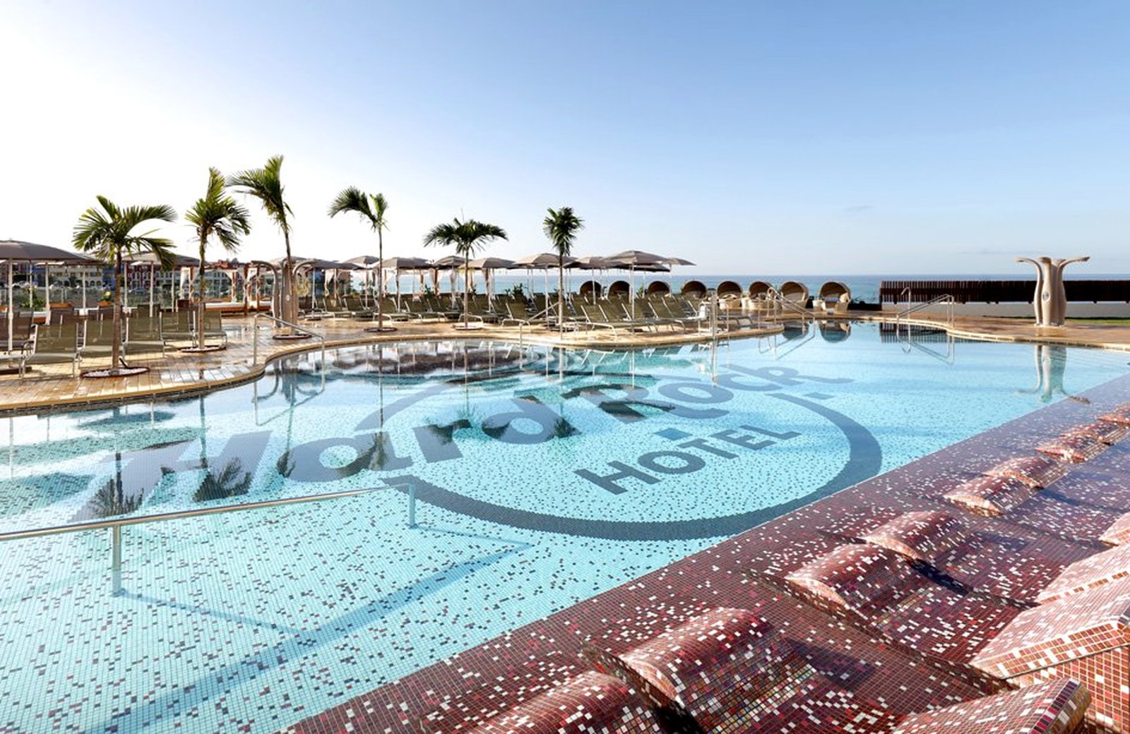 The main pool at Hard Rock Hotel Tenerife, tiled with the Hard Rock logo, with sun loungers and palms around it and the sea beyond.