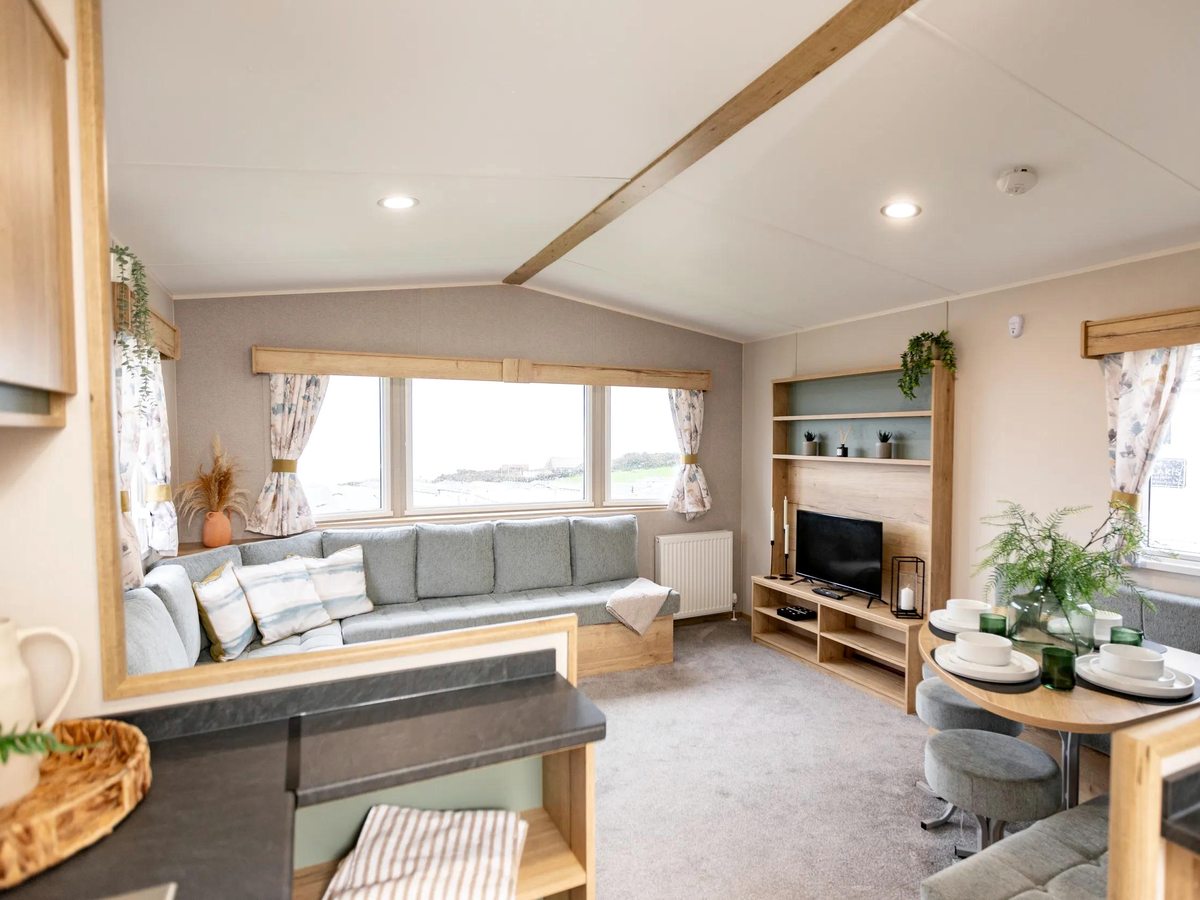 A spacious lounge with a vaulted ceiling, a long sofa, a media unit and a dining table by the windows.