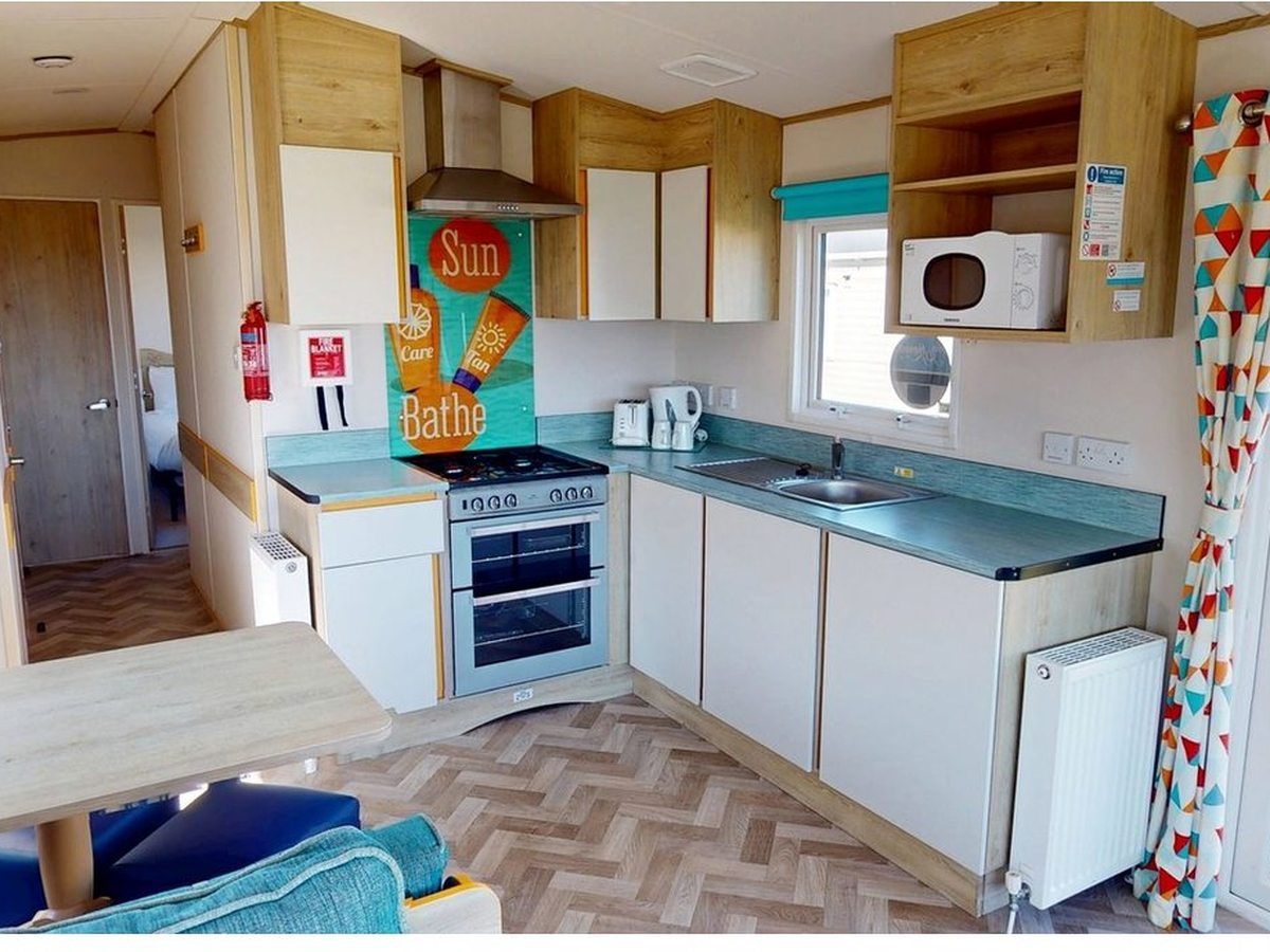 A caravan kitchen with an oven, hob, microwave and sink along an L-shaped worktop.