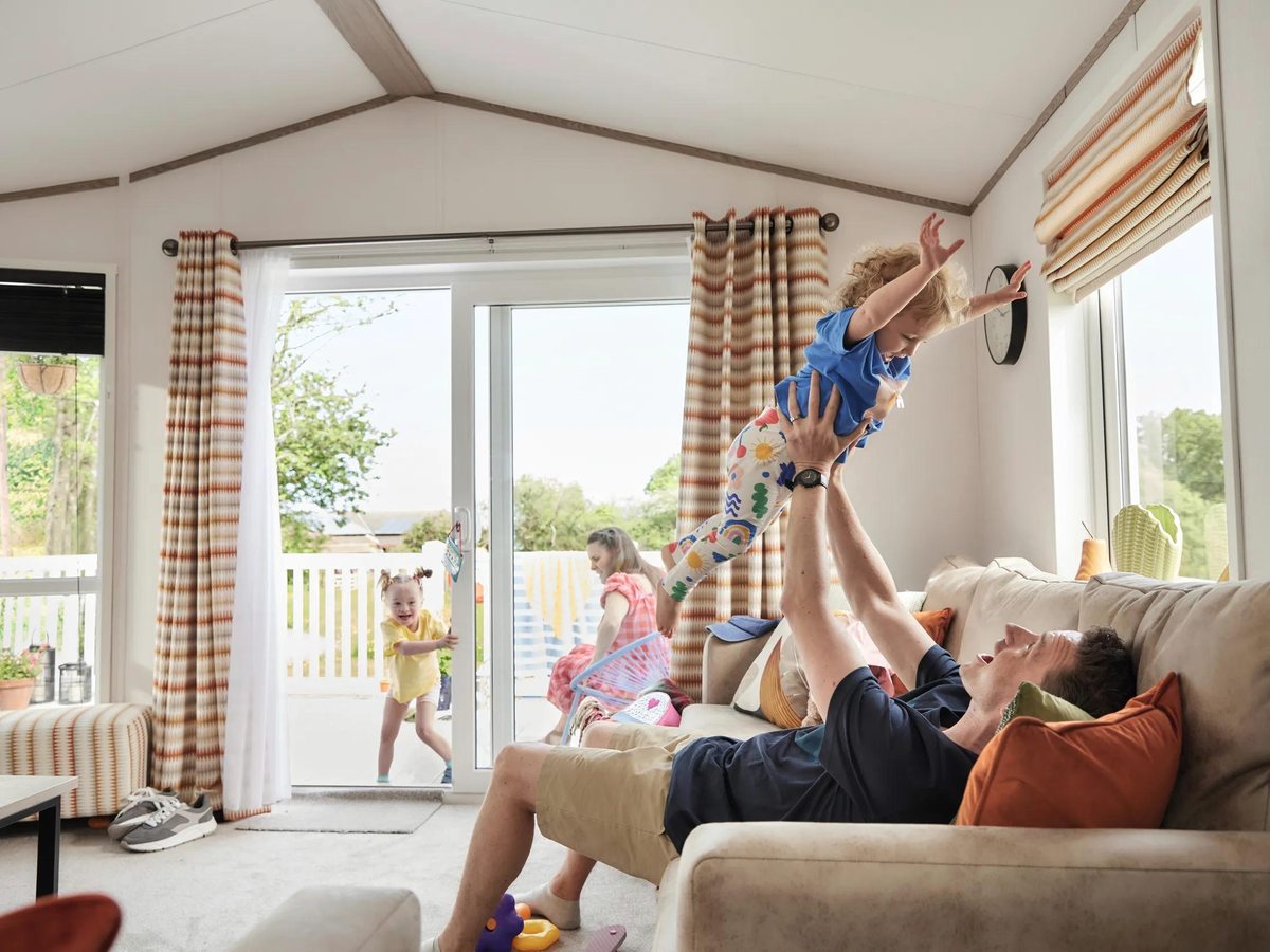 An open-plan living room with a sofa, curtains and patio doors opening onto the decking, a family relaxing inside.