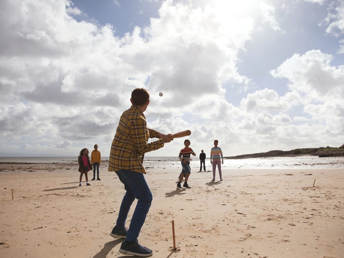 A family playing cricket on a wide sandy beach under a cloudy sky.