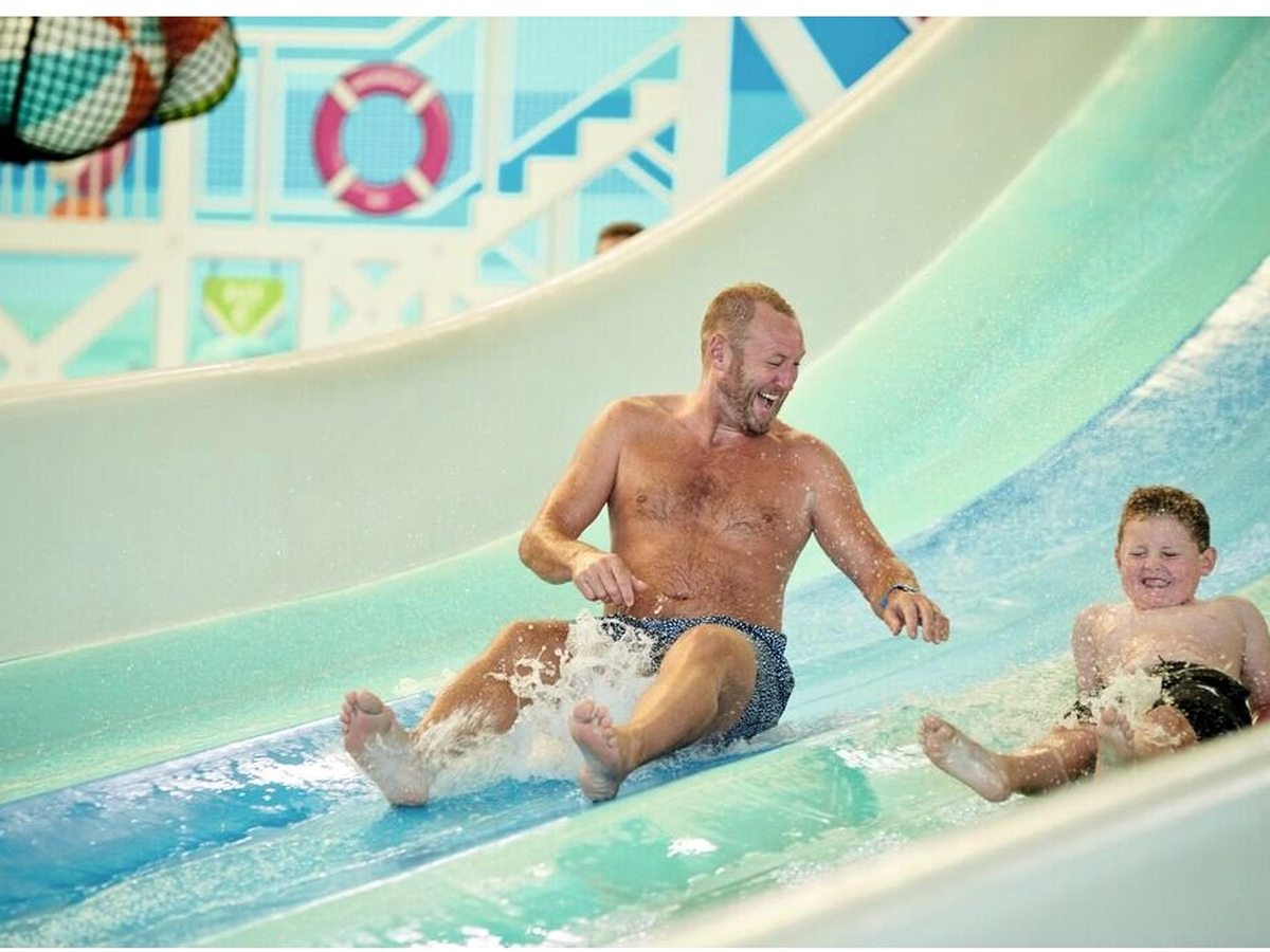 An adult and a child sliding down a pale-blue flume into the splashdown pool.