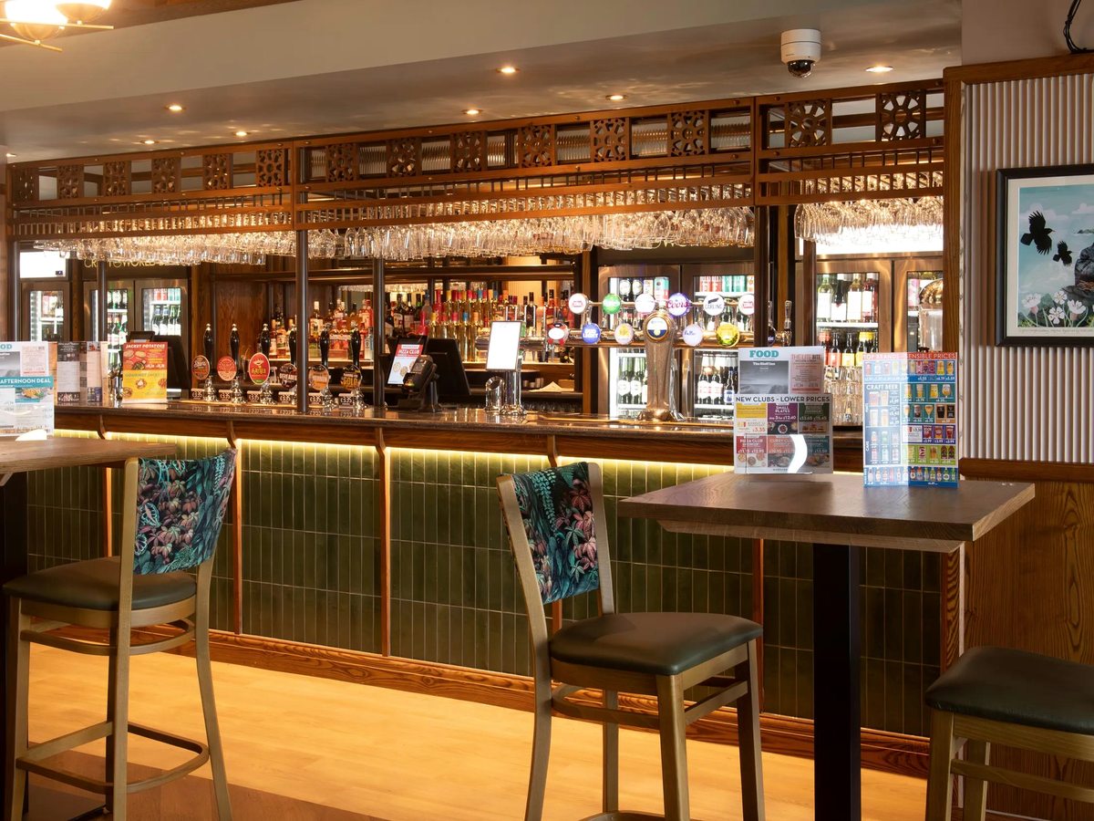 A long wood-and-green-tiled bar with cask ale pumps, bottle fridges and tall stools.