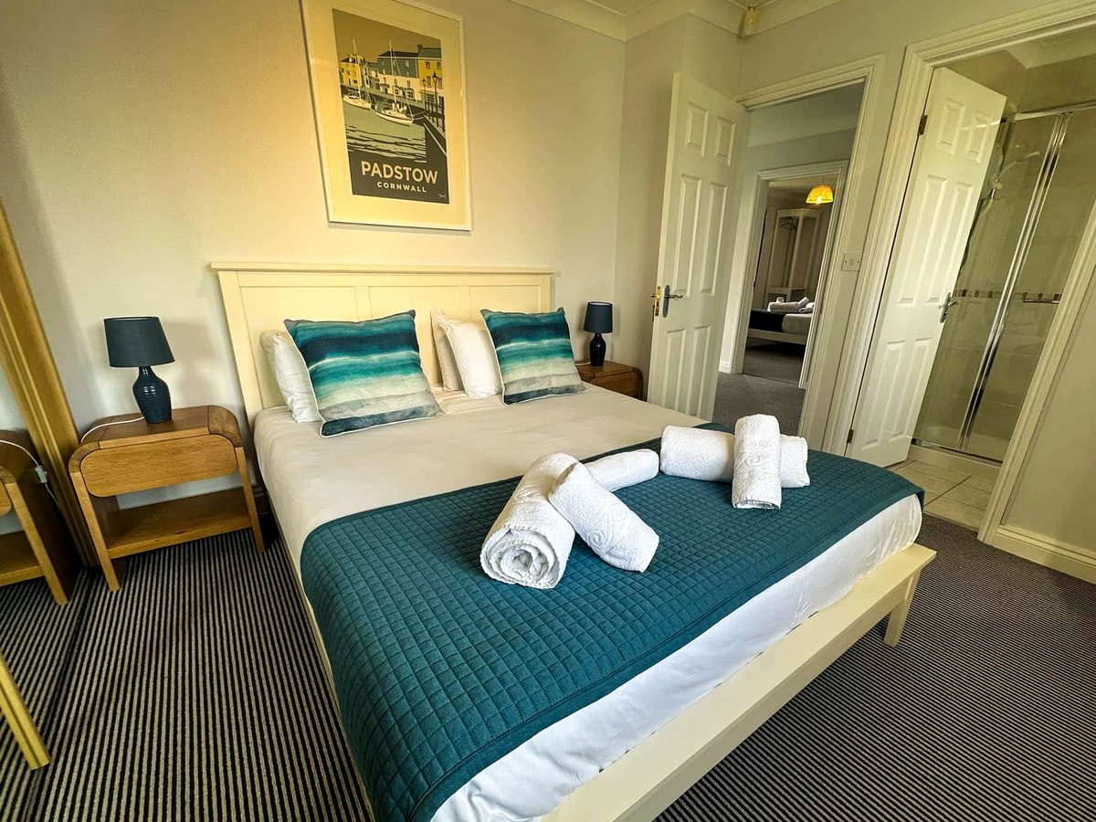 A double bedroom with a teal runner and cushions, towels folded on the bed and an en-suite shower room through an open door.