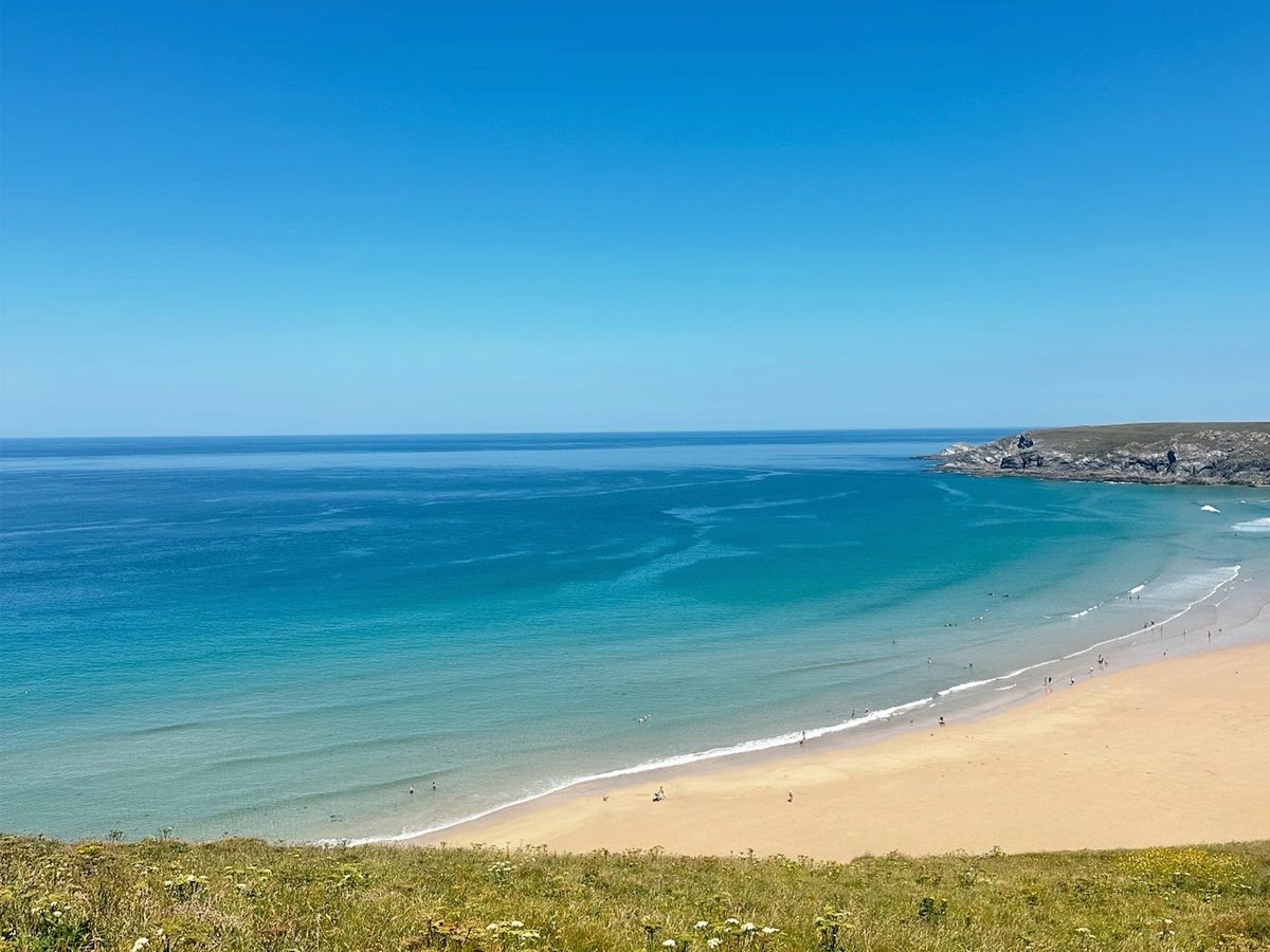 A broad sweep of golden sand and turquoise sea below grassy clifftops.