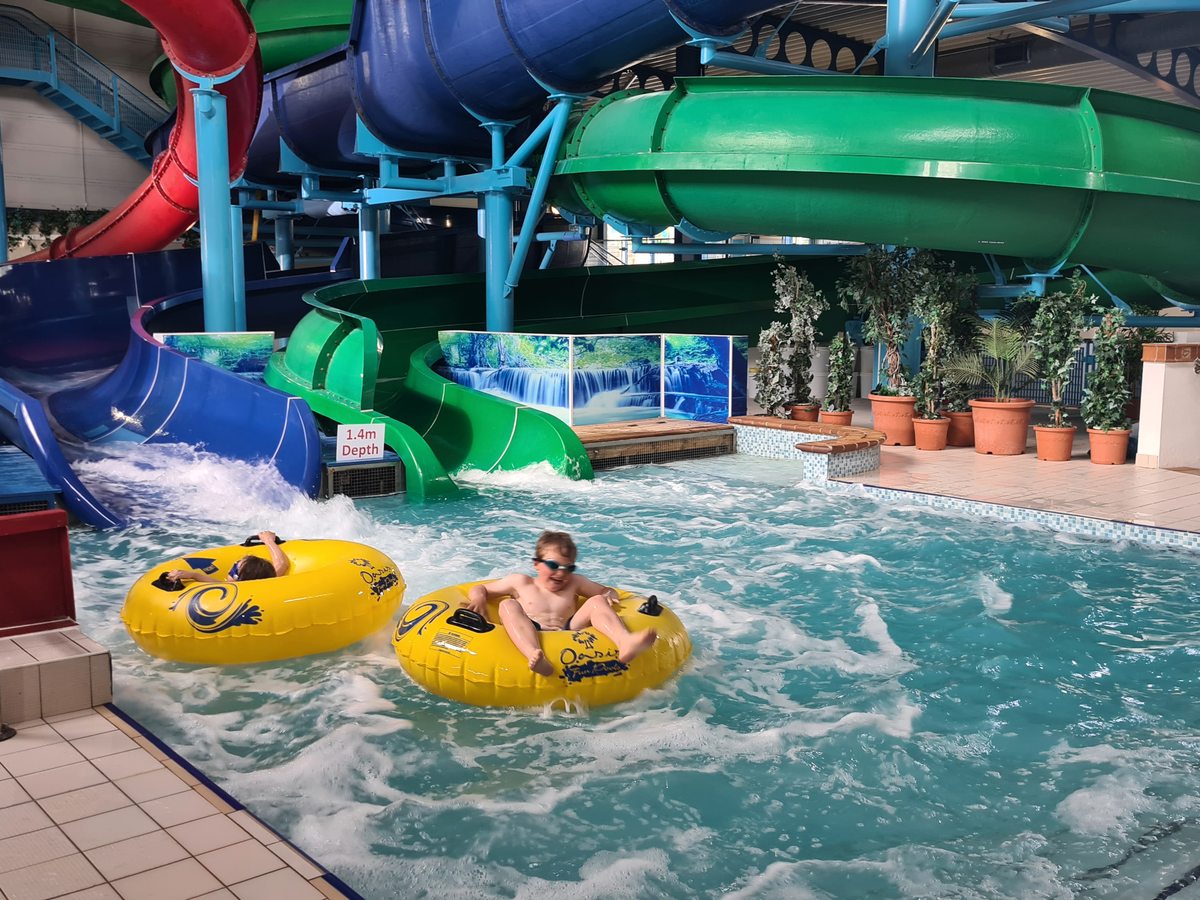Green and blue enclosed water flumes with a rider on a yellow ring reaching the splashdown pool.