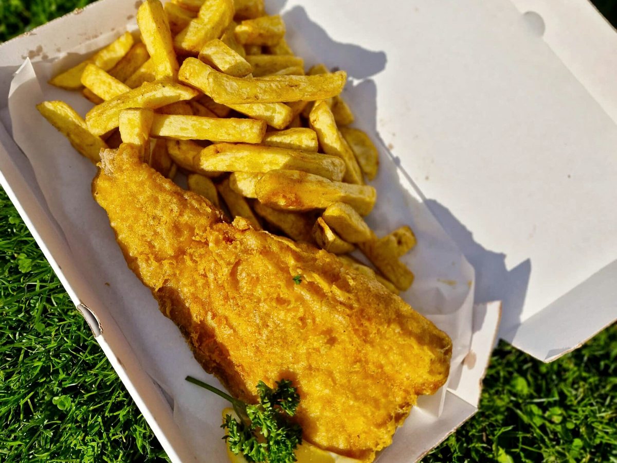 A takeaway box of battered fish and chips resting on grass.