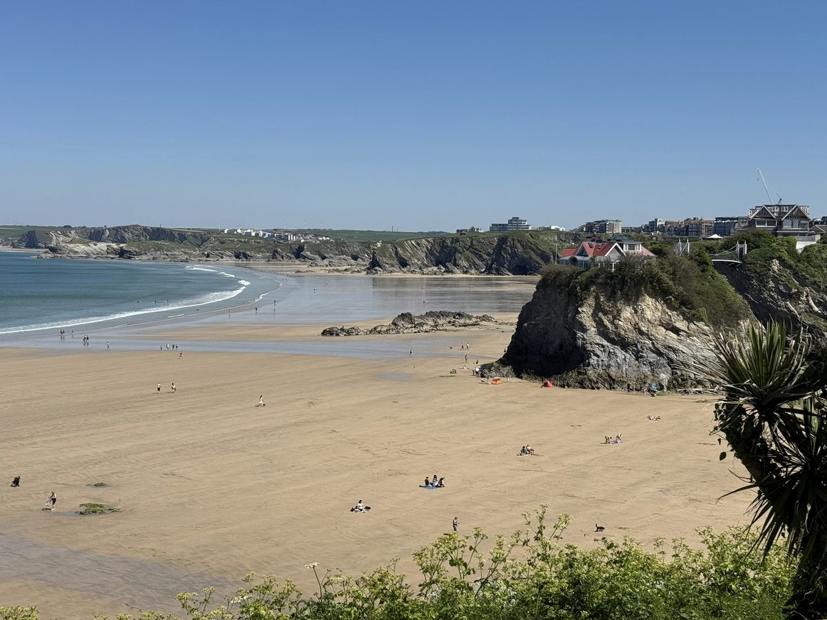 A wide sandy beach curving below the Newquay headland with the town on the cliffs above.