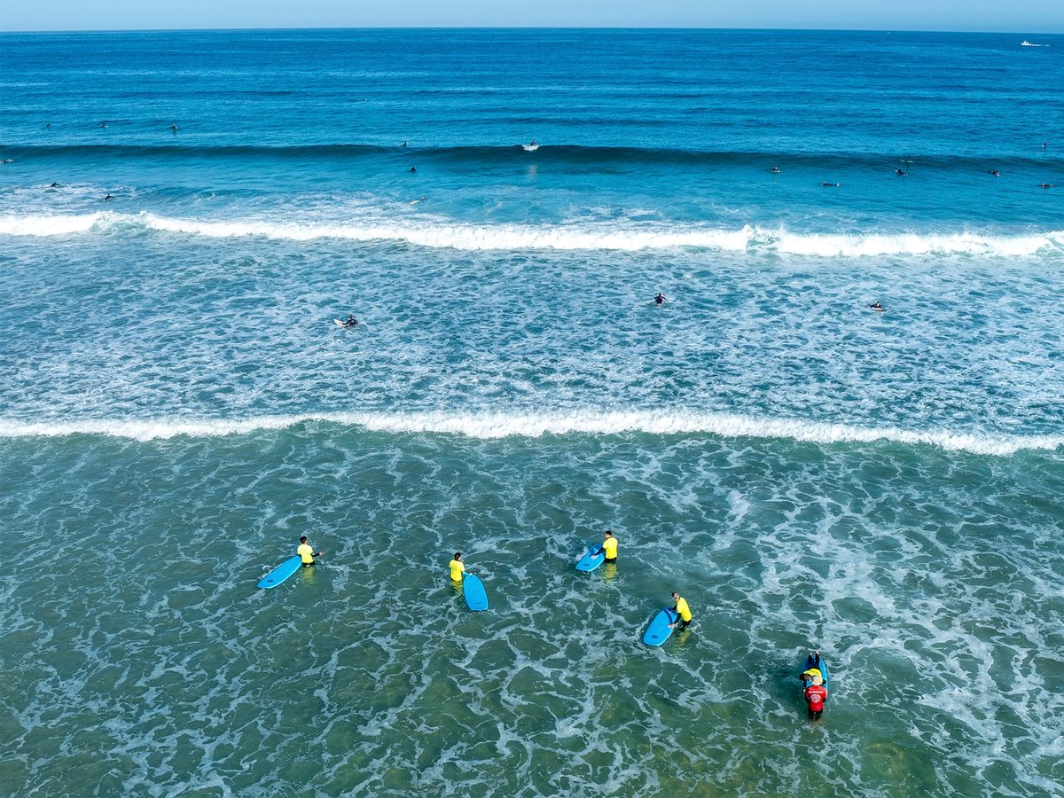 Surfers in yellow rash vests among the whitewater of small Atlantic waves.