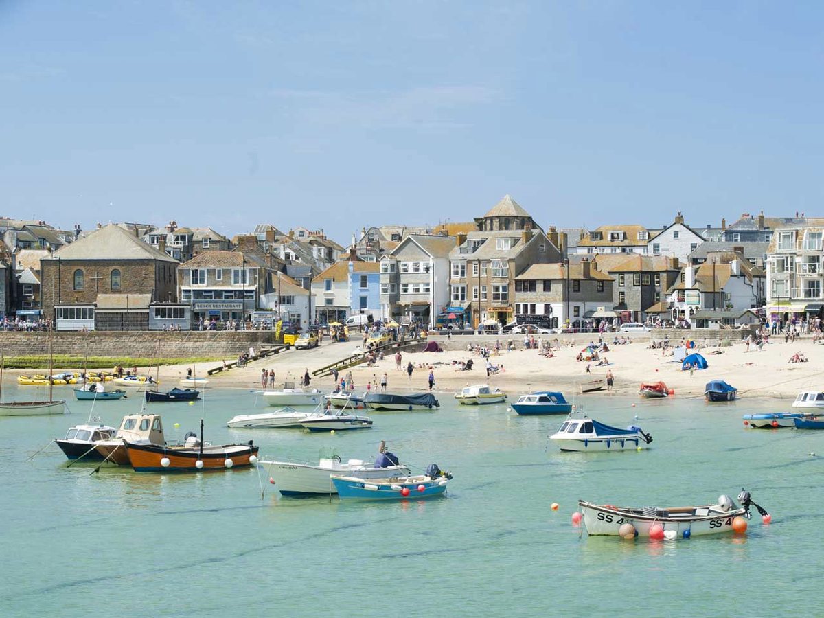 St Ives harbour with fishing boats on turquoise water and the town rising behind.
