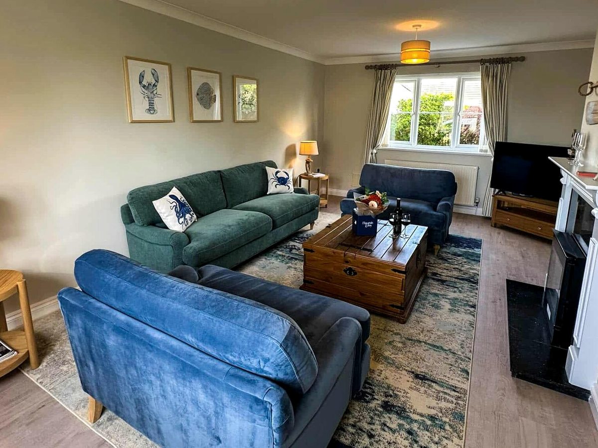 A spacious lounge with a green sofa, blue velvet sofa, wooden trunk coffee table and coastal-themed prints.