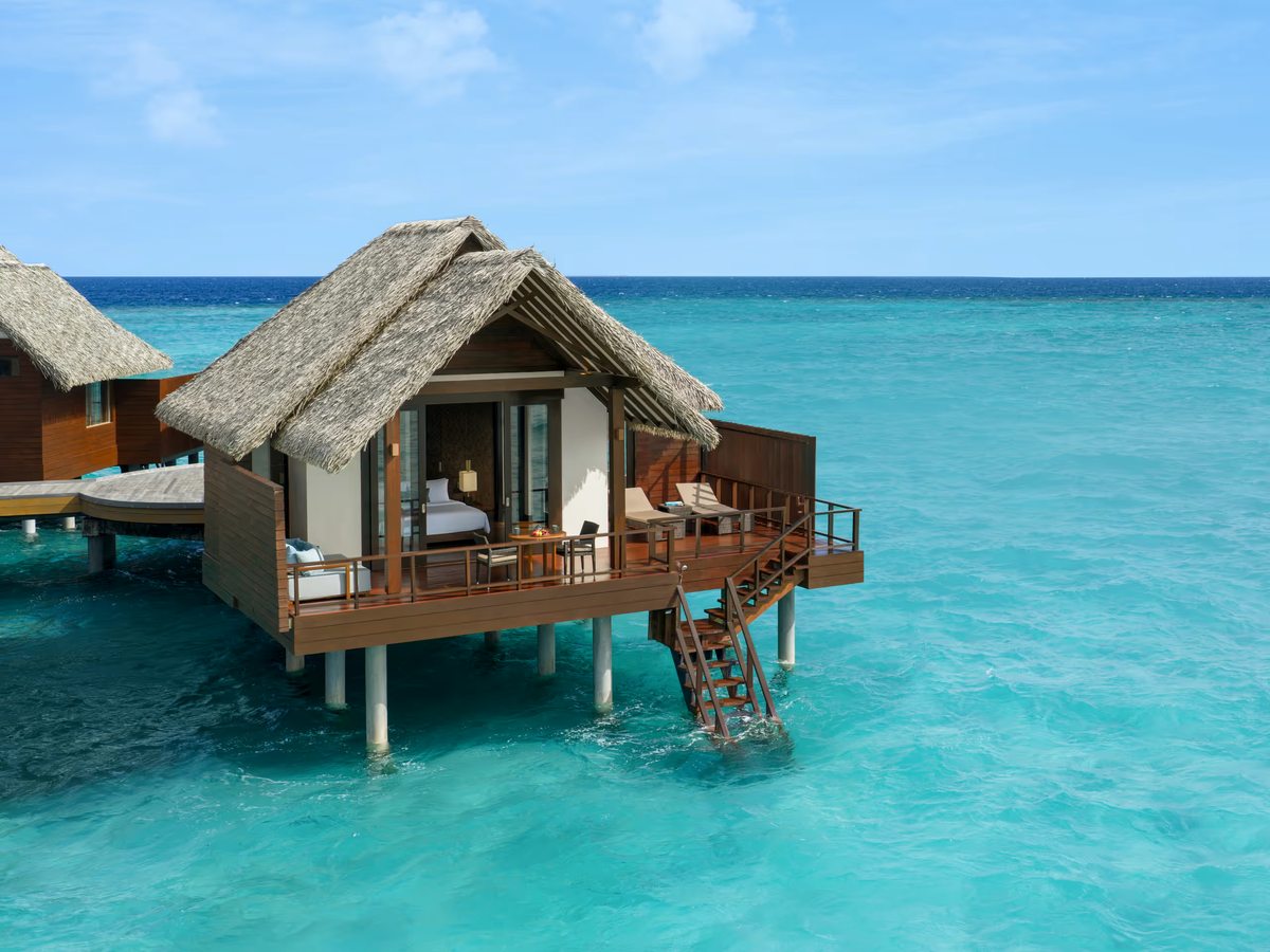 A thatched overwater villa on stilts above turquoise water, with a private deck and steps down to the sea.