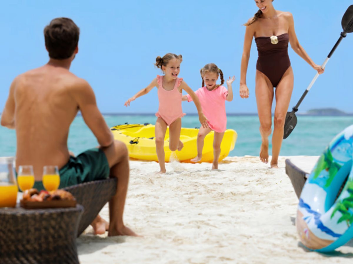 A family on the white-sand beach beside yellow kayaks, with the calm turquoise lagoon behind.