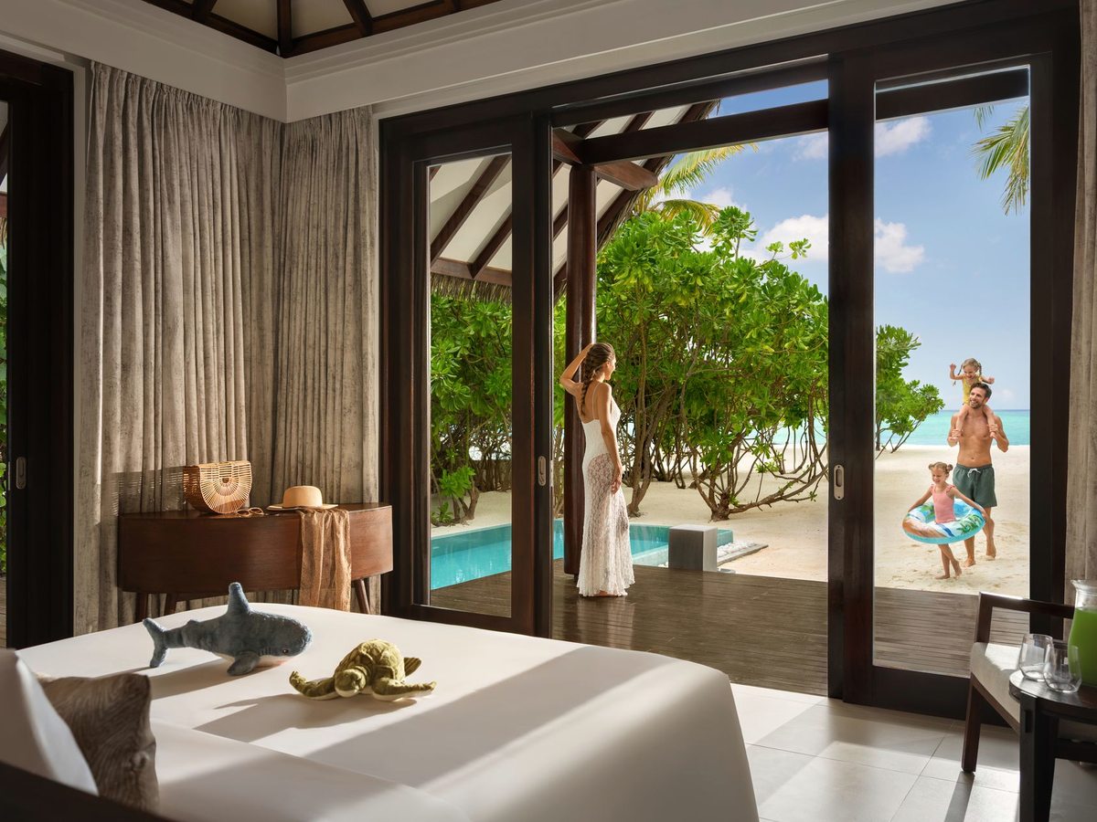 A villa bedroom opening onto a timber deck with a private plunge pool, a fruit platter on the bed and greenery beyond.