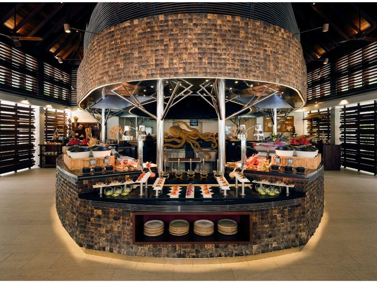 A large central buffet island with a stone base and a hanging wine display under a domed woven-shade light, ringed by serving counters.