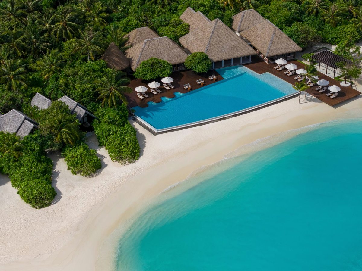 A large freshwater pool with loungers and parasols under palms, set just behind the white-sand beach and turquoise lagoon.