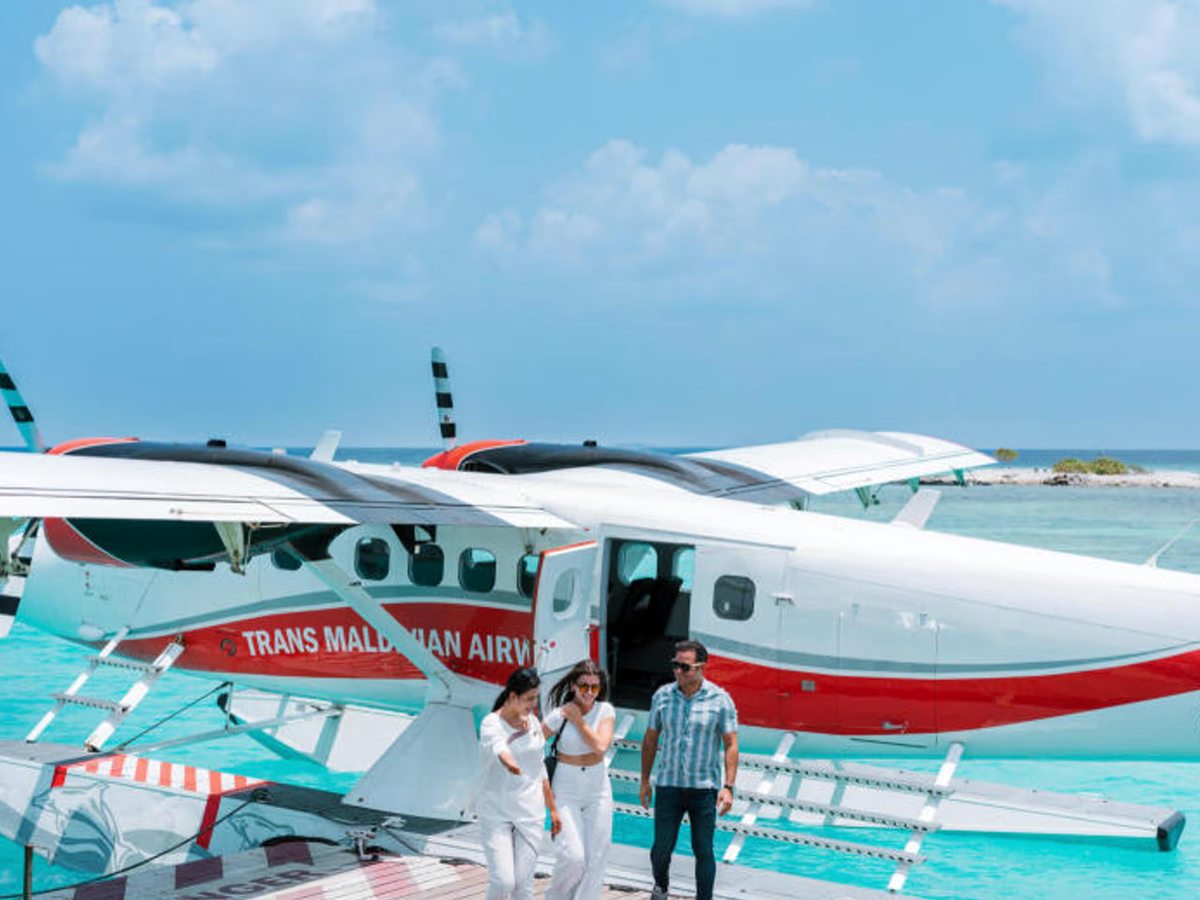A red-and-white seaplane moored at a jetty as guests step ashore onto the deck.