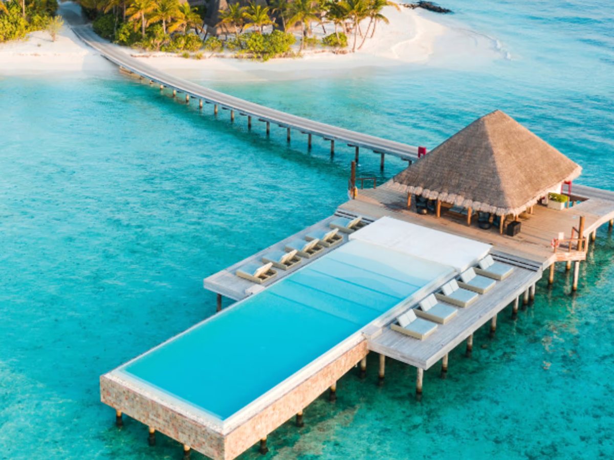 An overwater infinity pool beside a thatched bar at the end of the jetty, edged with daybeds over the turquoise lagoon.