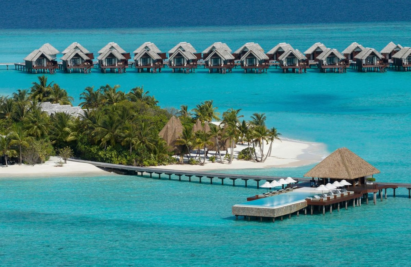 Heritance Aarah, a private-island resort in the Maldives: a long row of thatched overwater villas over a turquoise lagoon beside the palm-covered island.