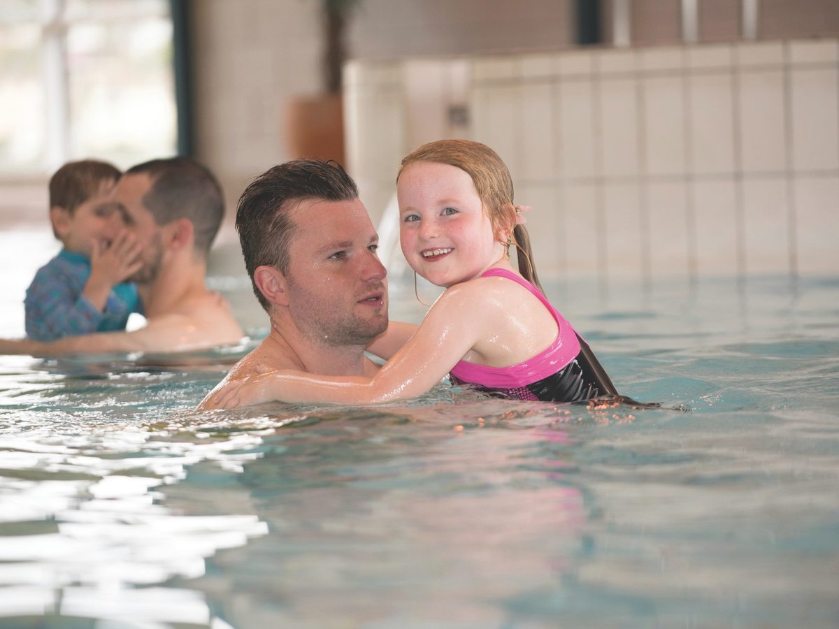 A father and young daughter standing in the shallow water of the indoor leisure pool.