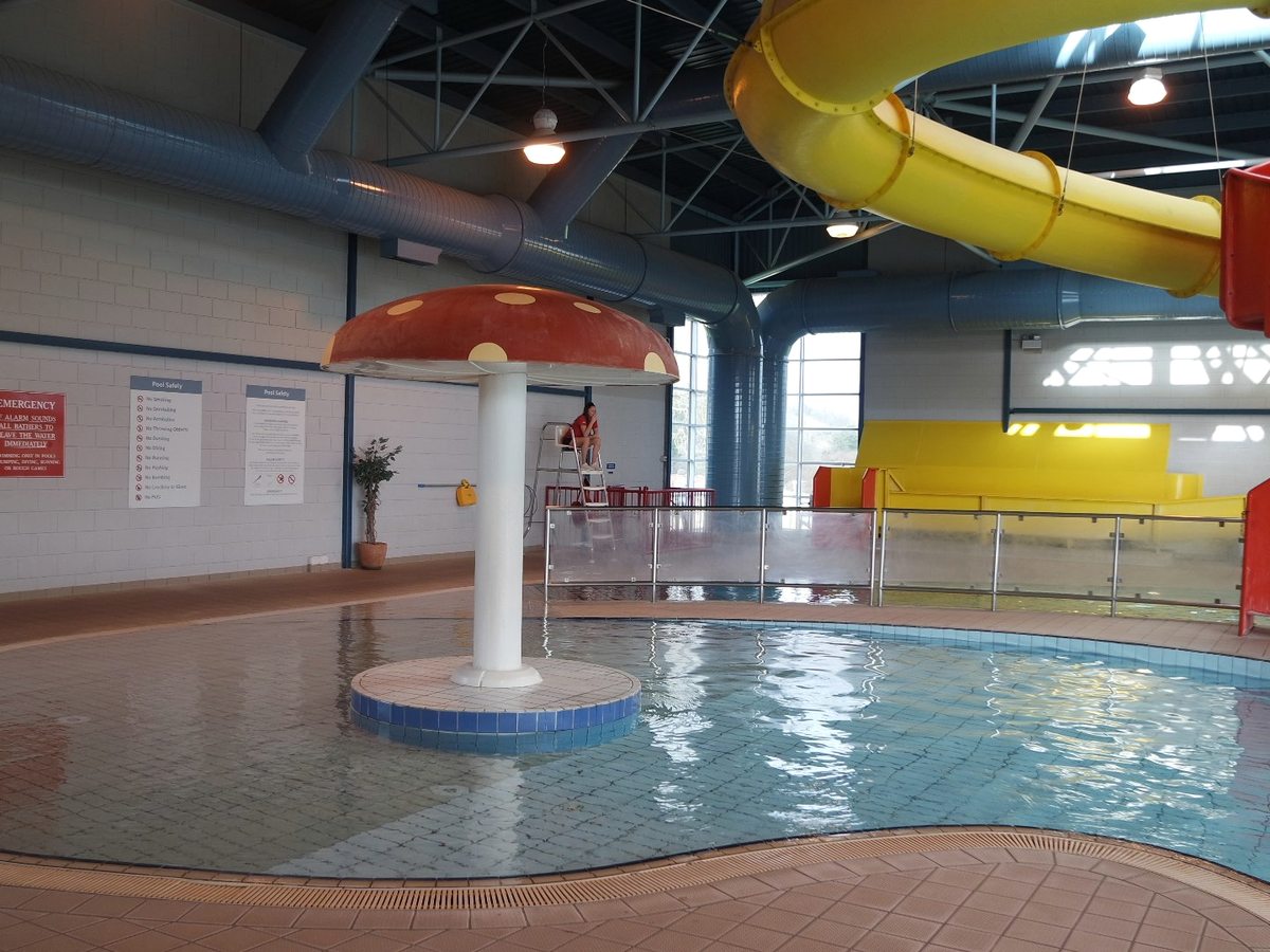 A mushroom splash feature and a yellow flume slide winding down into the indoor pool hall.