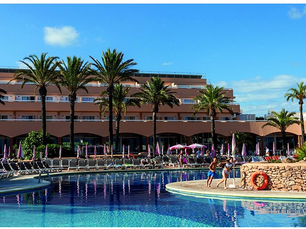 The large main pool ringed by loungers and umbrellas below the resort's salmon-coloured low-rise blocks and tall palms.