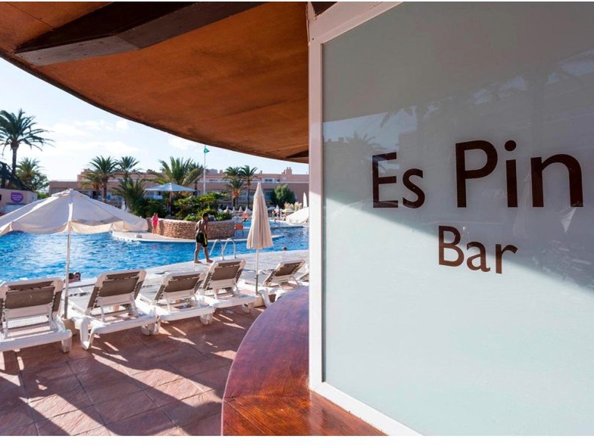 The Es Pins Bar sign above a poolside snack bar, with parasols, loungers and the pool alongside.