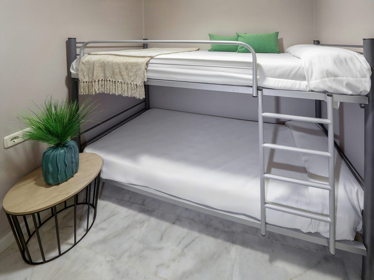 Bunk beds with a guard rail and ladder against a marble-tiled wall, with a small planted side table alongside.