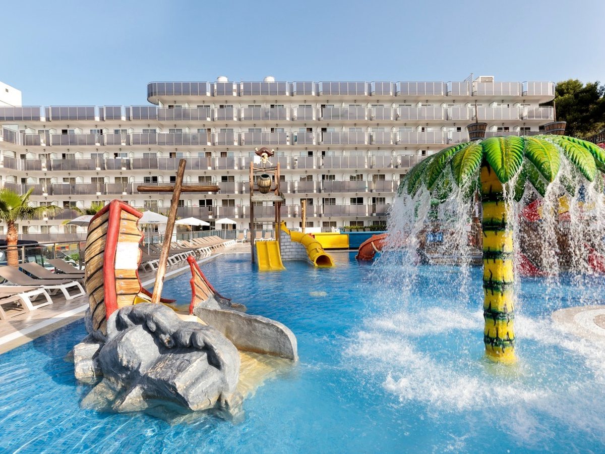 A splash pool with a wooden pirate ship and a tall palm-shaped water feature spraying into the water, the hotel behind.