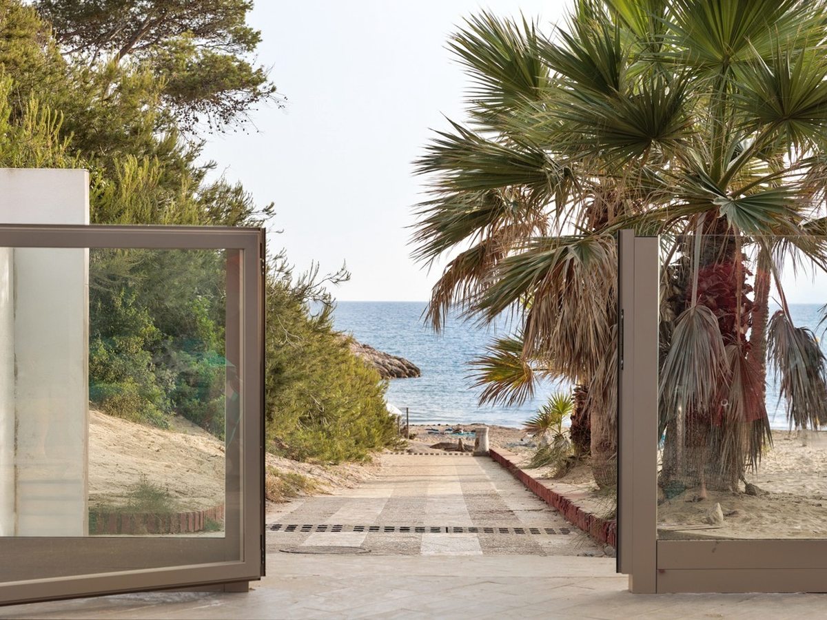 A paved path descending between palms toward the sandy cove and the sea.