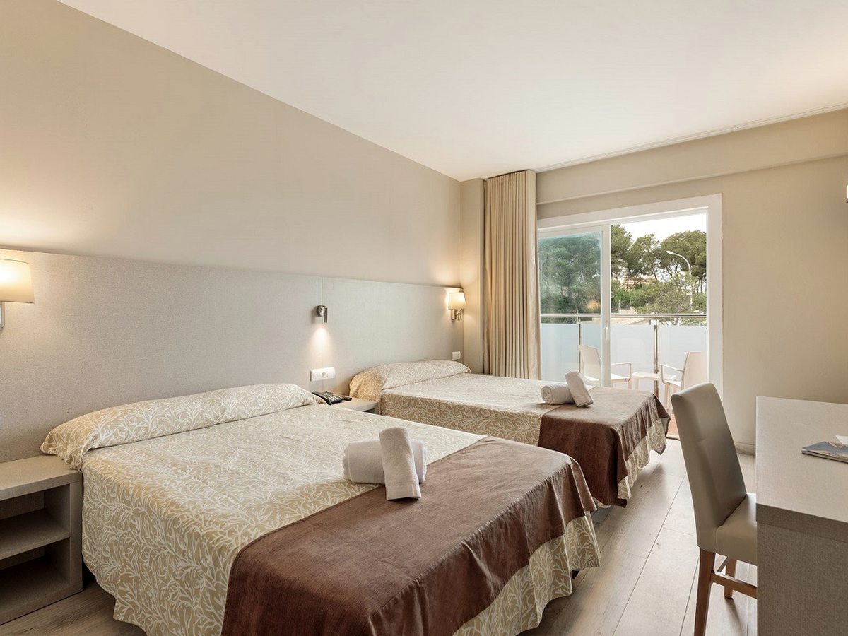 A room with two queen beds dressed in cream and brown, a window to the trees.