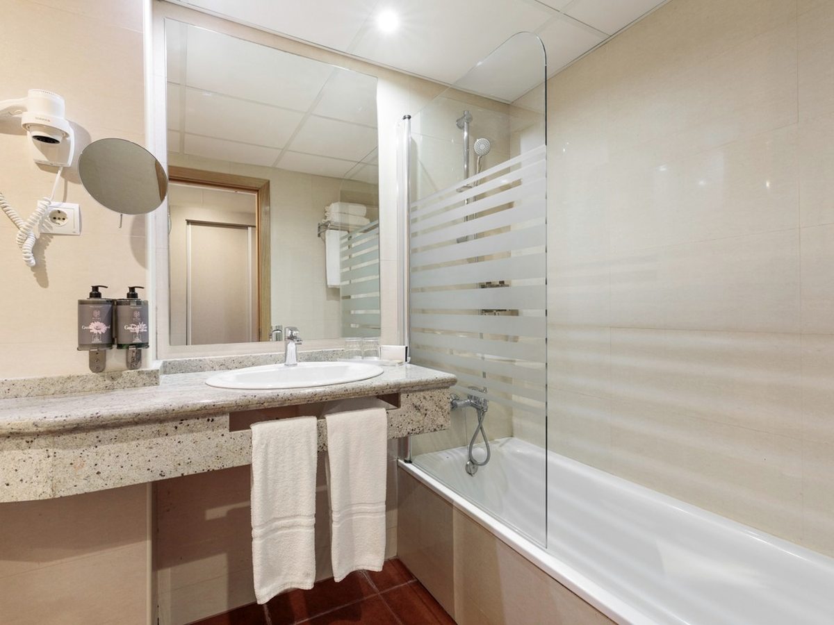 A bathroom with a granite-topped vanity, a mirror and a bath with an overhead shower.