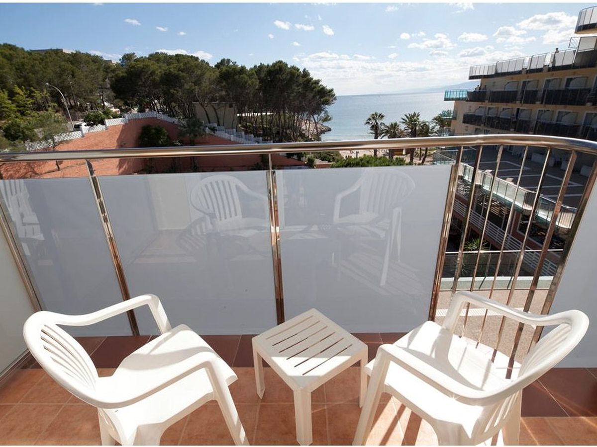 A tiled room terrace with white chairs and a table behind a glass balustrade.