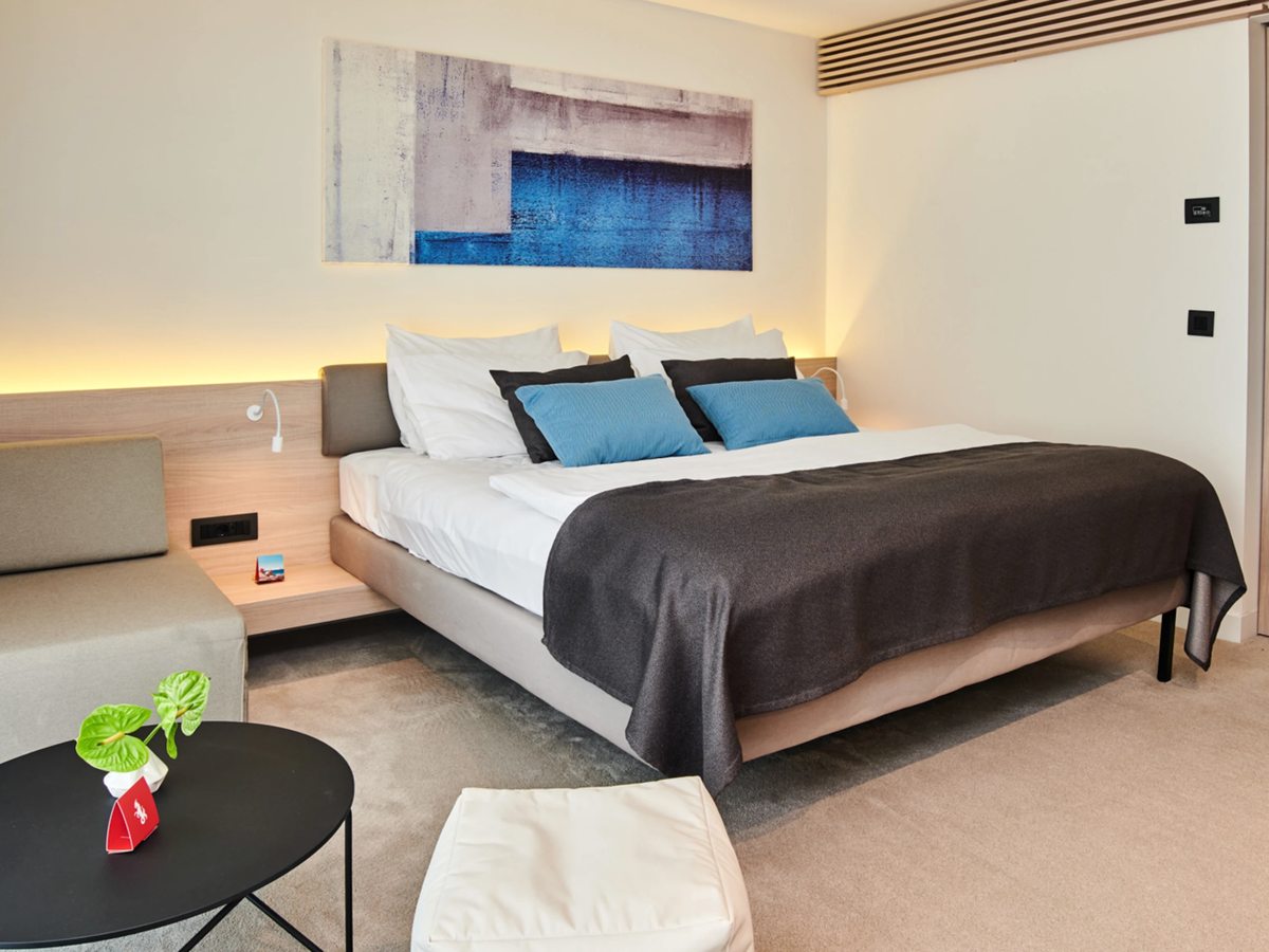 A double room with a king bed, a grey padded headboard, blue and charcoal cushions and an abstract blue artwork above the bed.