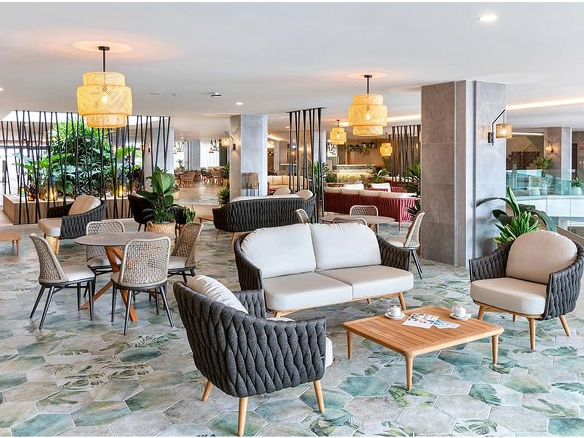 The resort's open-plan lobby lounge with wicker sofas and armchairs, pendant lights and a leaf-patterned tiled floor.