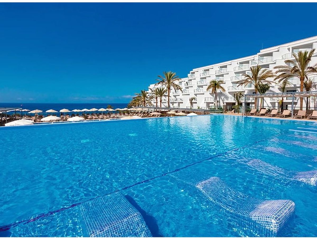 An infinity pool whose edge meets the sea view, with tiled in-water sun loungers and palms along the far side.